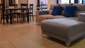 A modern living room with a grey sofa, two blue cushions, and a dining area with wooden chairs and a small table.