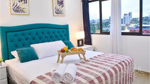A hotel room with a large bed, a tray with breakfast items, and a city view through the window.