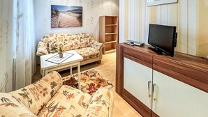 Ett vardagsrum med en soffa, ett soffbord, en tv som står på ett skåp och en bokhylla.