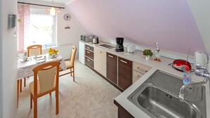 A kitchen with a sink, stove, and microwave. There is a dining table with chairs and a window with curtains. - Ferienwohnung Neukloster (Neukloster)