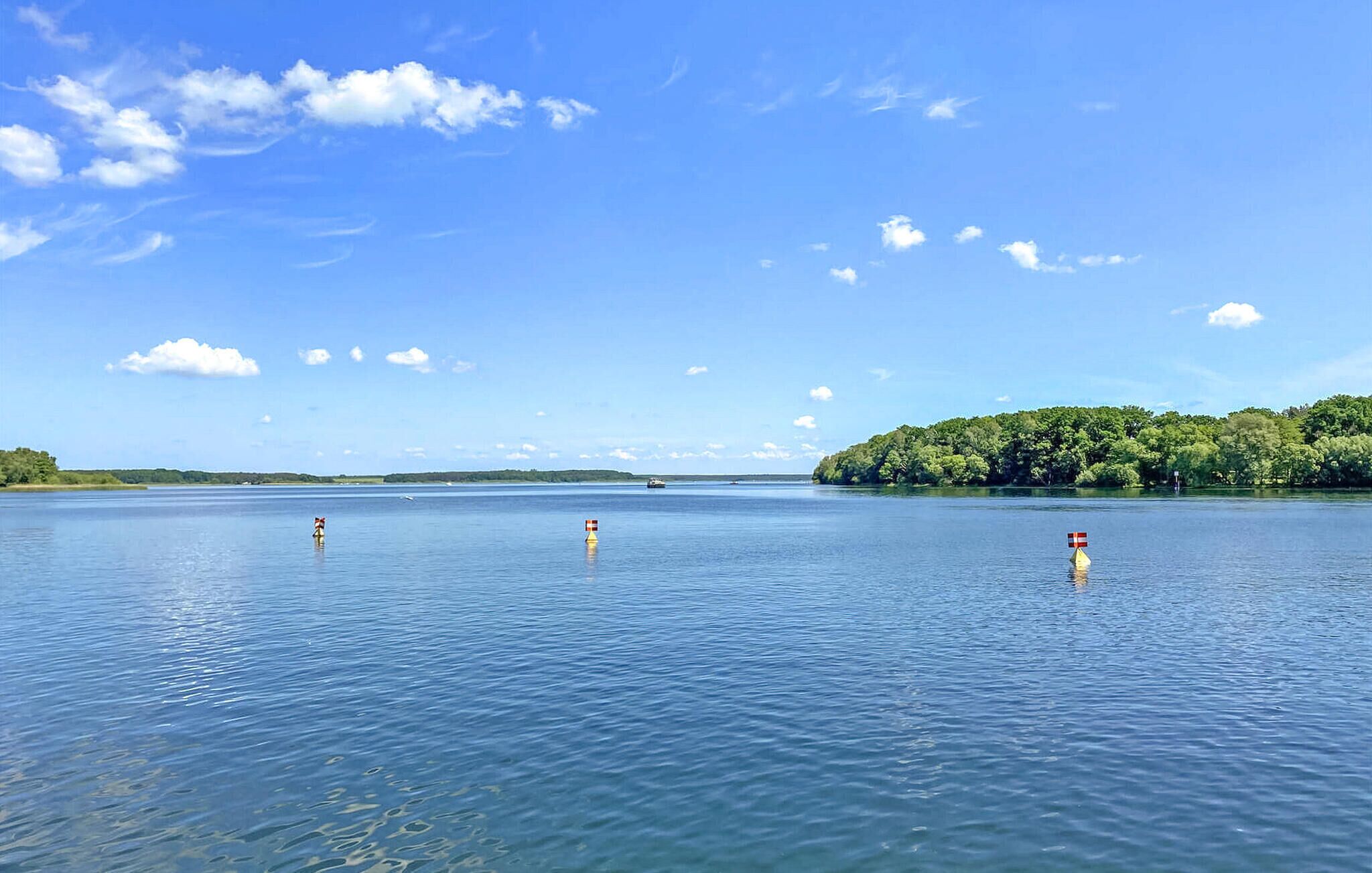 A calm lake with three buoys and a small island with dense greenery in the background.