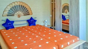 A bed with an orange bedspread, two blue pillows, a bedside lamp, and a decorative fan on the wall. - Ferienhaus Ueckermünde Bellin (Ueckermünde OT Bellin)