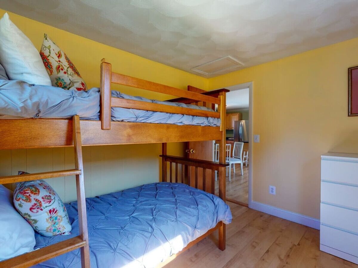 Habitación con literas, cabecera de madera, cómoda blanca y una silla al fondo.