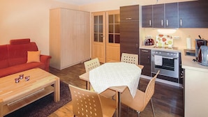 Un espace de vie compact comprenant un canapé, une table à manger avec des chaises, une kitchenette équipée d’un four et d’une machine à café, ainsi qu’une armoire aux portes vitrées.