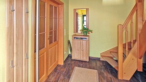 Un couloir avec des portes en bois, une petite armoire, un tapis et un escalier.