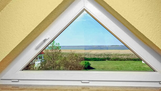Une fenêtre de toit triangulaire offrant une vue sur un champ verdoyant et une côte lointaine.