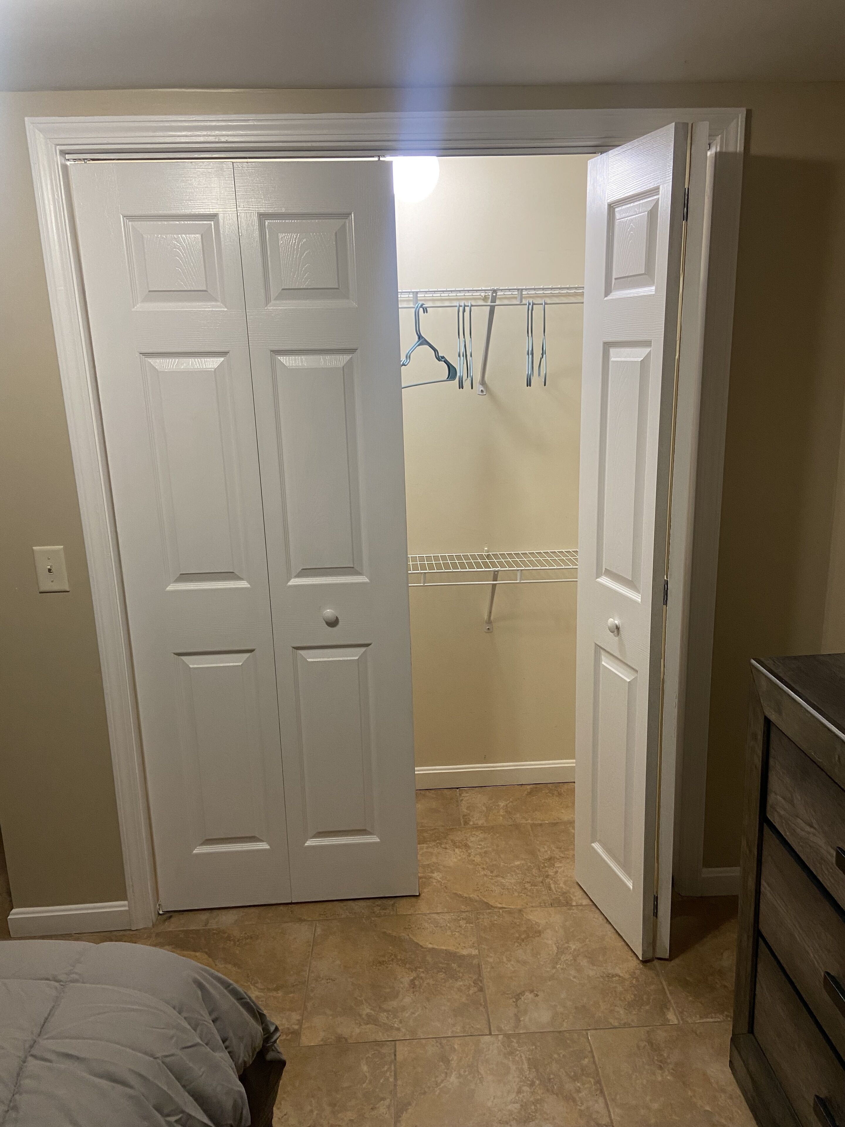 Quarto com armário fechado, cama e closet espaçoso com roupas penduradas.