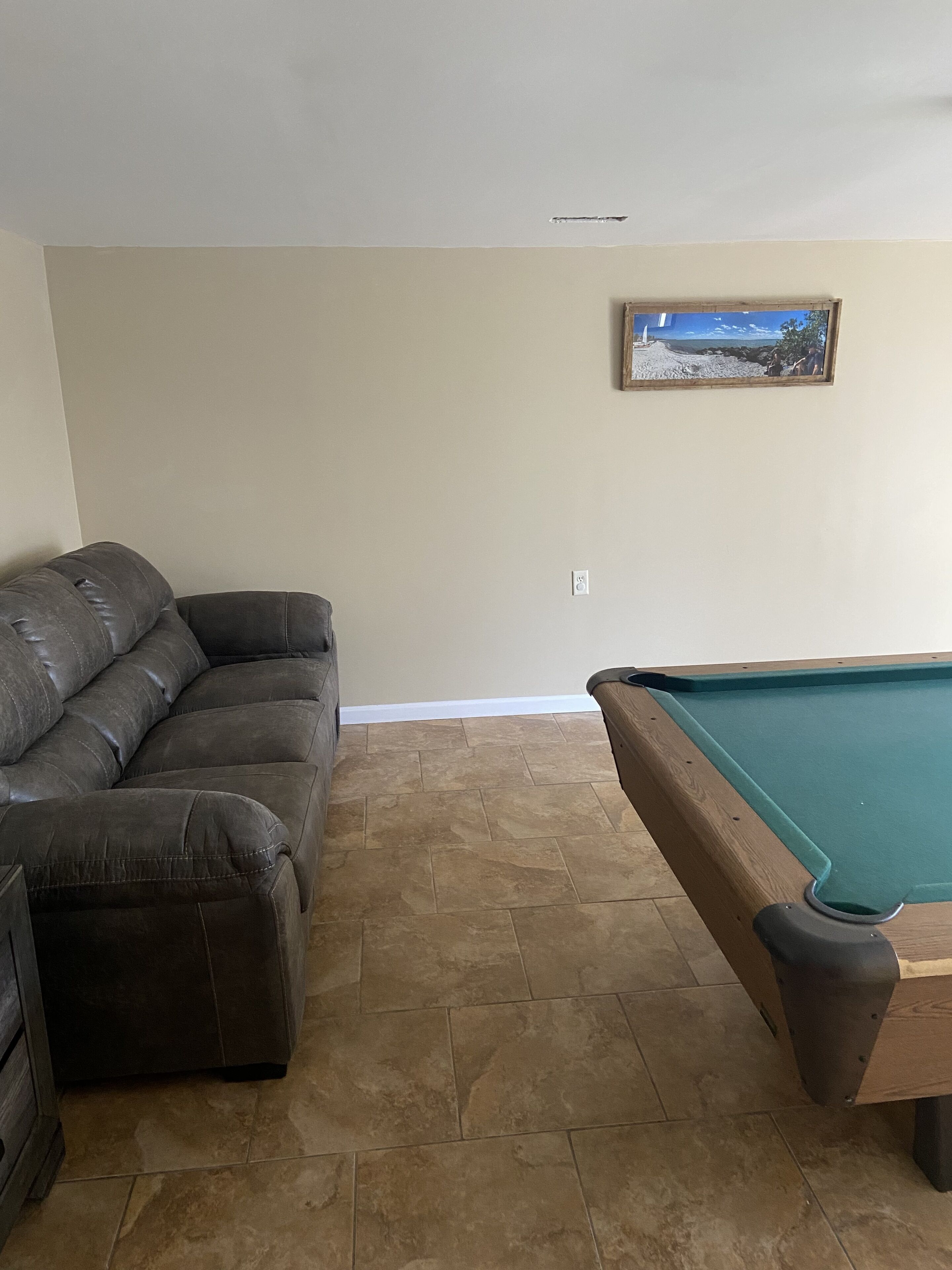 A living room with a dark brown leather sofa, a pool table, beige walls, and a framed picture on the wall.