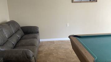 A living room with a dark brown leather sofa, a pool table, beige walls, and a framed picture on the wall.