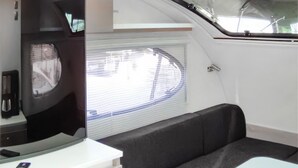 A compact living space with a television, a window with blinds, and a small seating area.