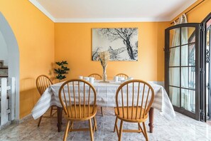 Une salle à manger avec une table mise pour quatre personnes, un vase contenant des fleurs séchées et un grand tableau accroché au mur.