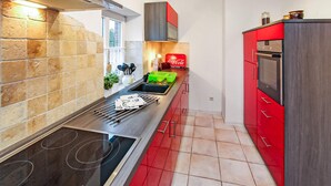 Una cocina moderna con una placa de inducción negra, armarios rojos y salpicadero de azulejos.