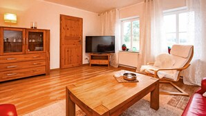 Una sala de estar con una mesa de centro de madera, un televisor sobre un mueble bajo, un sofá rojo, un sillón blanco y un aparador de madera con puertas de vidrio.