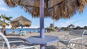 A beachside seating area with a thatched umbrella, metal chairs, and a view of the sea.