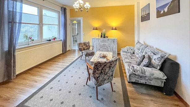 En stue med sofa, spisebord med stole, lysekrone og radiator.