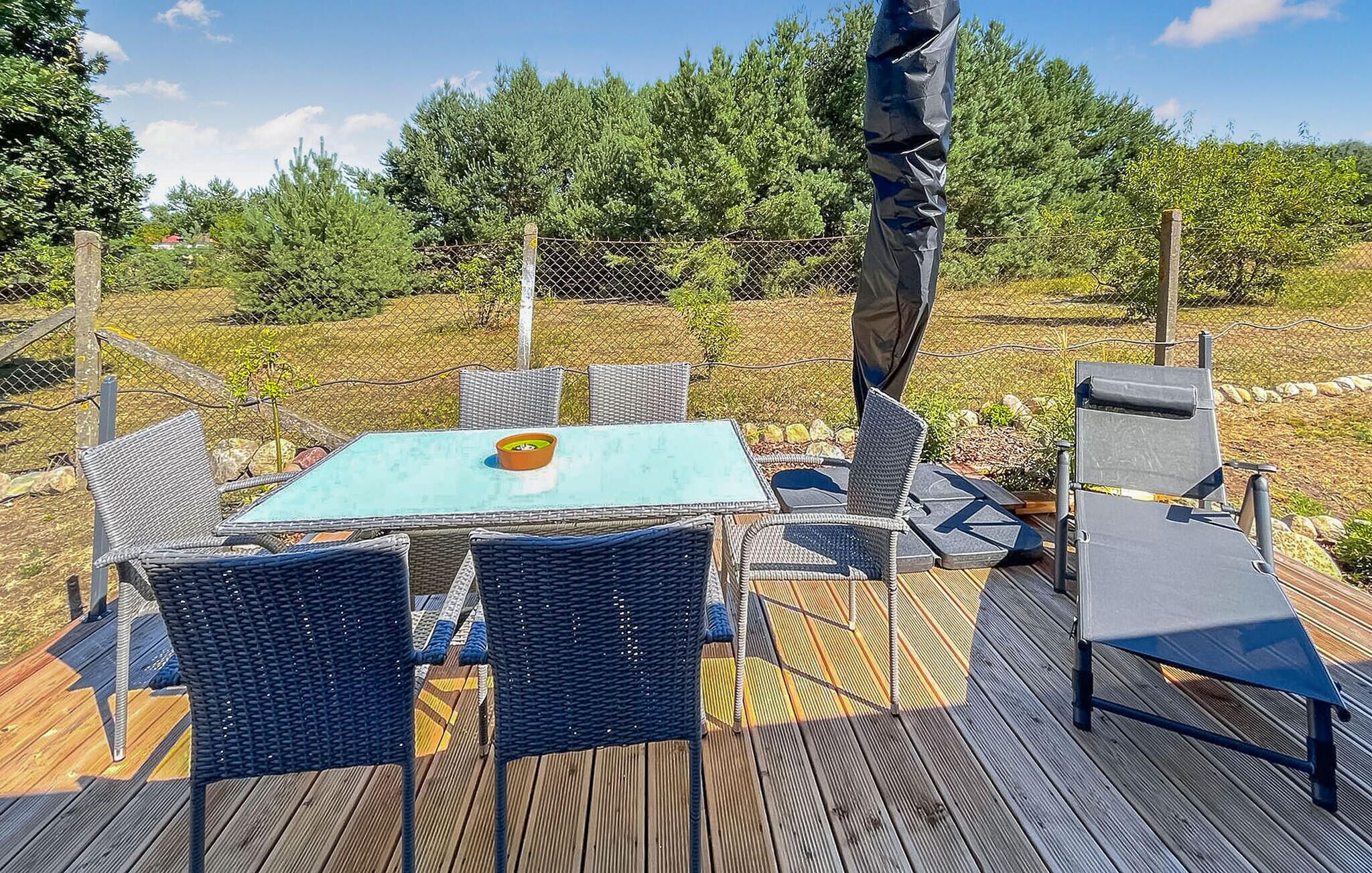 An outdoor patio with a table and chairs, surrounded by a wooden deck and a chain-link fence.