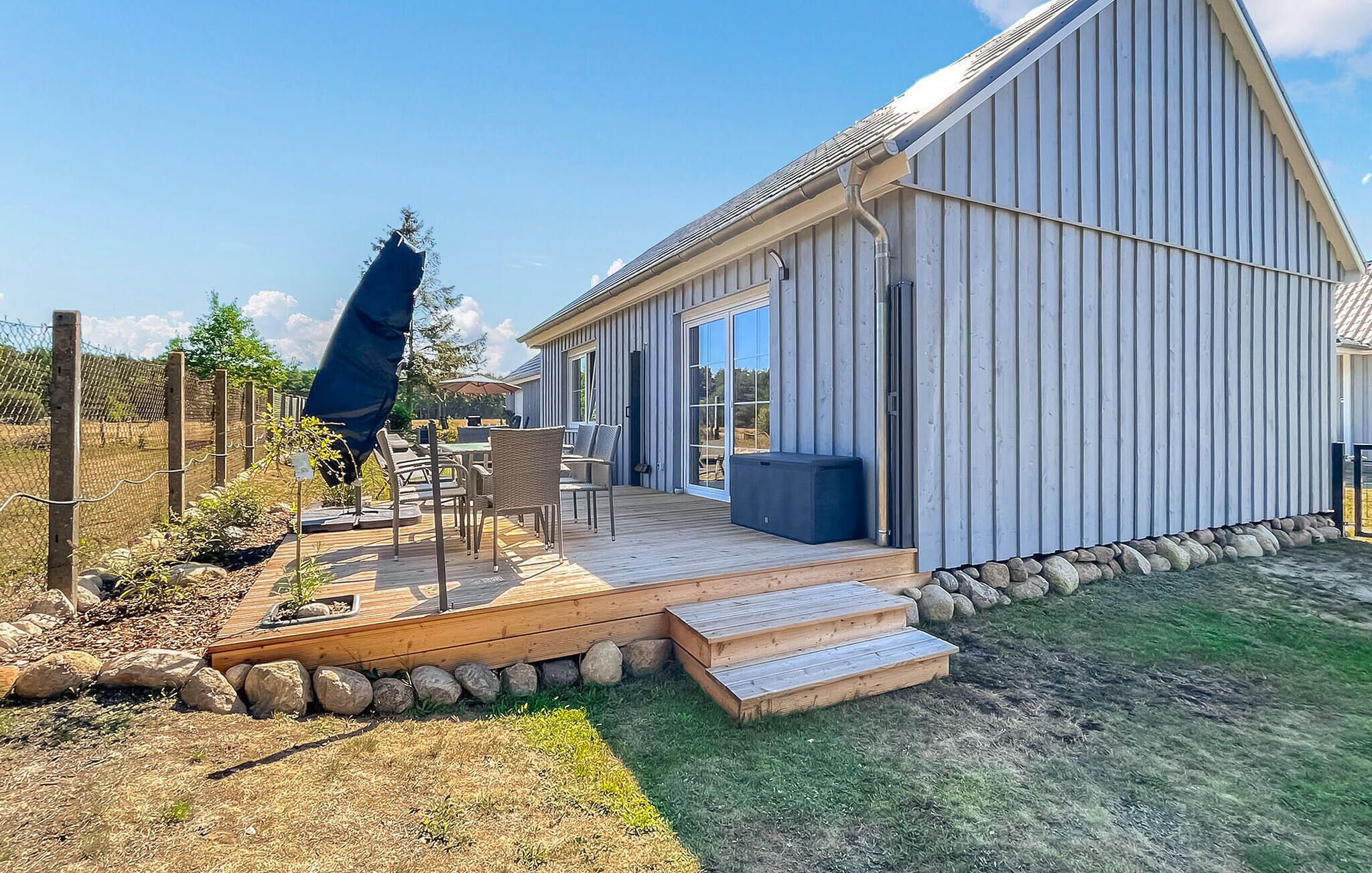 Ein modernes Haus mit einer großen Terrasse, Sitzgelegenheiten im Freien und einer Steinmauer.
