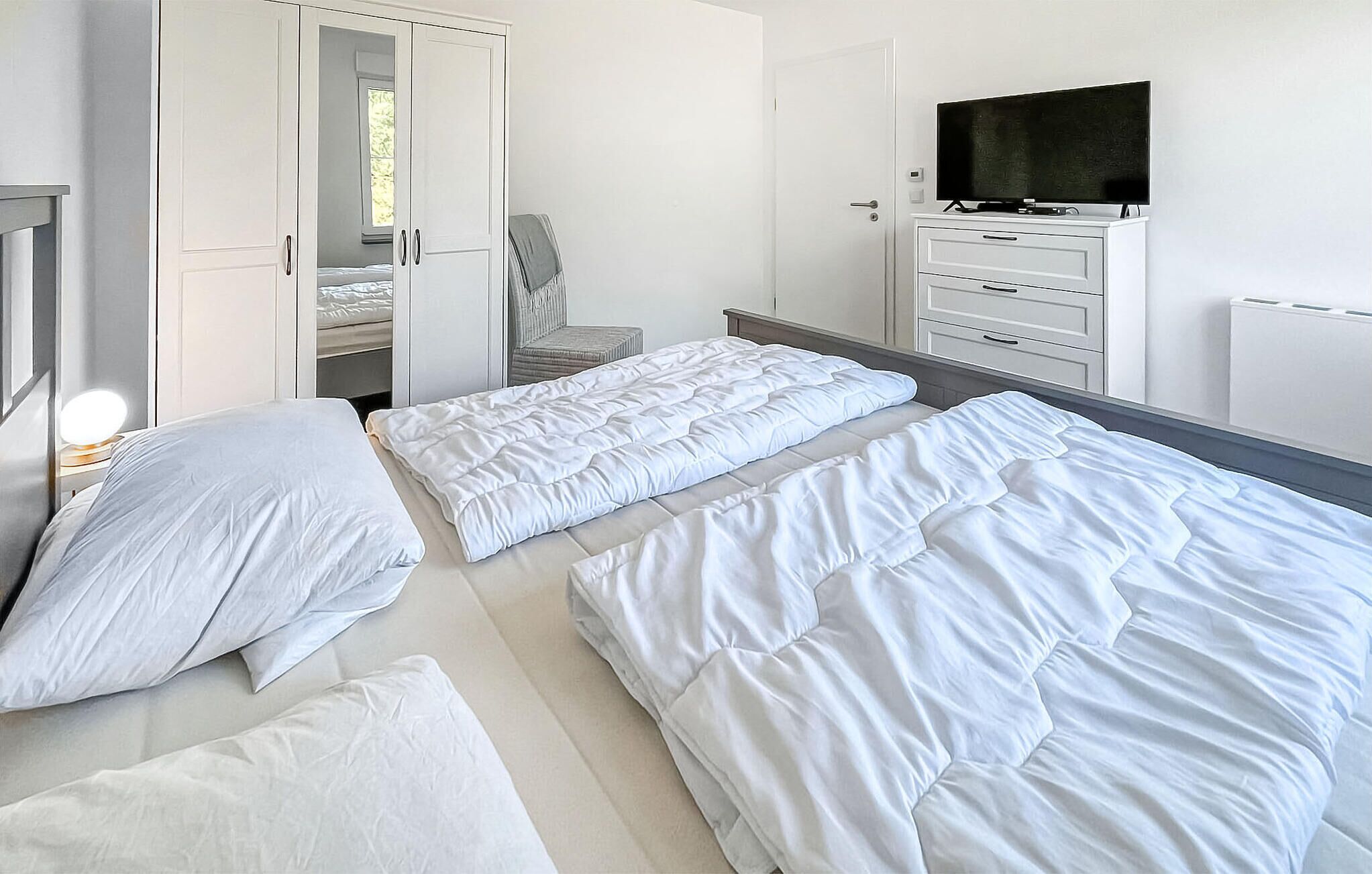 A bedroom with two beds, a TV, a wardrobe, and a chair.