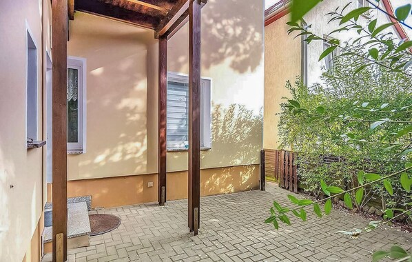 A covered outdoor area with a brick floor, wooden posts, and a small step leading to a door.