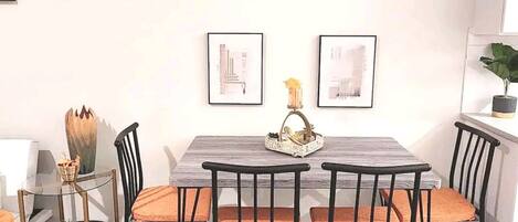 Un comedor con una mesa rectangular, cuatro sillas y dos cuadros en la pared.