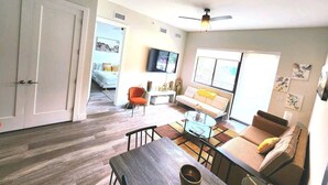 A spacious living area with a sofa, coffee table, and a dining table. There is a television mounted on the wall and a ceiling fan. - Lux and Cozy 2beds 2 Baths up to 8 guest (West Palm Beach)