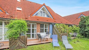 A house with a red-tiled roof, a brick exterior, and a wooden deck with outdoor furniture. - Ferienwohnung Prerow Ostseebad (Prerow (Ostseebad))
