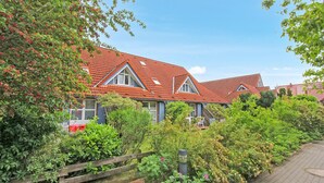 A row of houses with red tiled roofs, surrounded by lush greenery and a paved pathway. - Ferienwohnung Prerow Ostseebad (Prerow (Ostseebad))