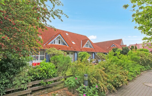 A row of houses with red tiled roofs, surrounded by lush greenery and a paved pathway. - Ferienwohnung Prerow Ostseebad (Prerow (Ostseebad))