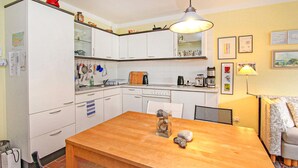 A compact kitchen with white cabinets, a wooden dining table, and a hanging light fixture. - Ferienwohnung Prerow Ostseebad (Prerow (Ostseebad))