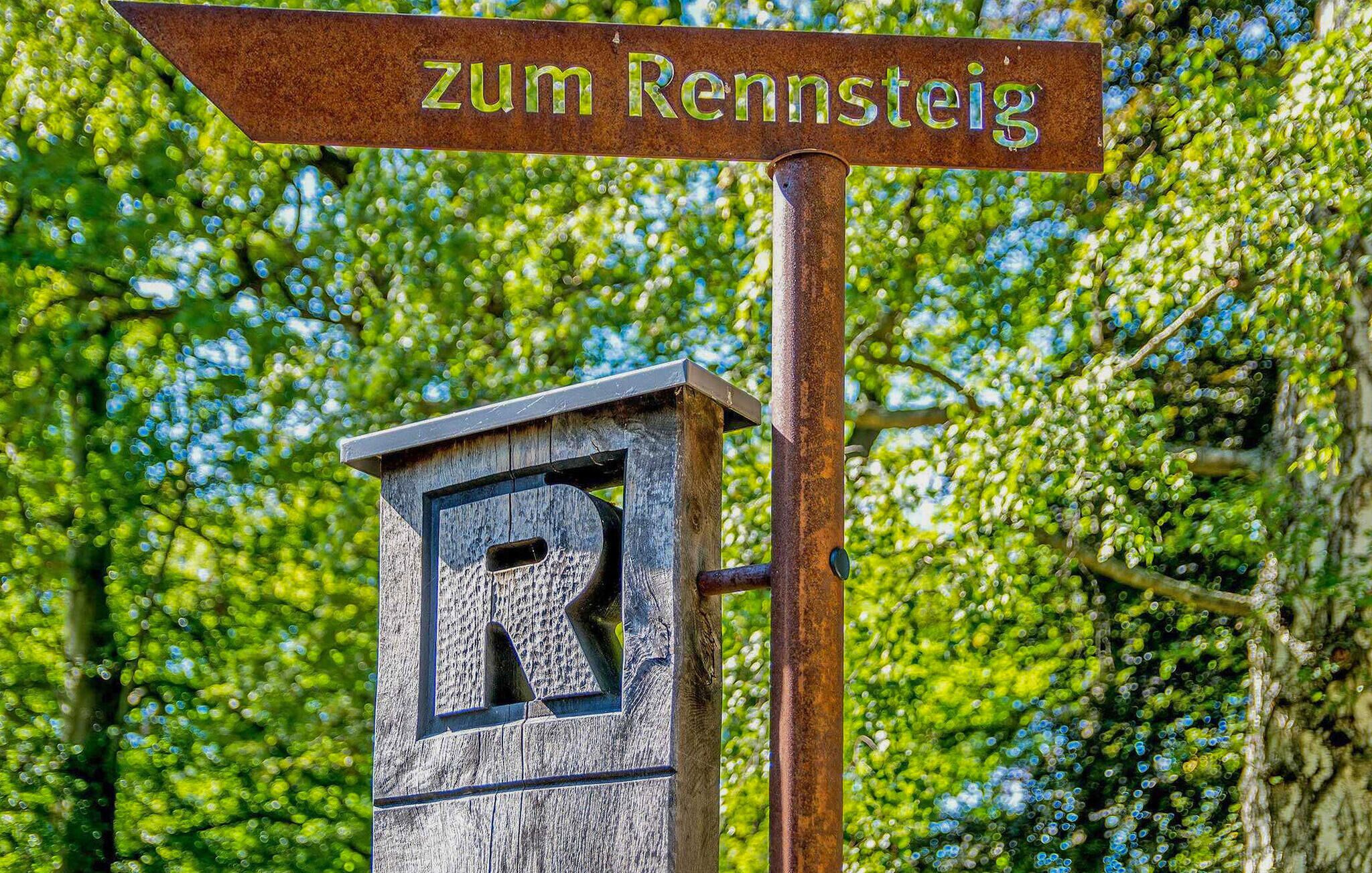 Un segnale stradale con la scritta 'zum Rennsteig' e una struttura in legno con una 'R'.