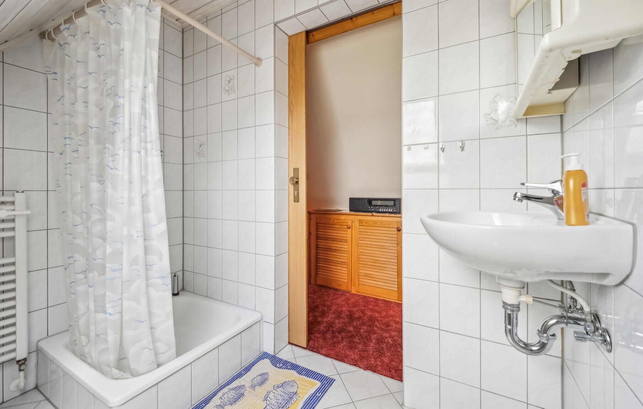 Een badkamer met een bad, douchegordijn, wit wastafel en een houten kastje.