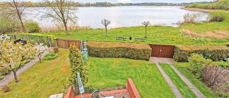 En trädgård med en uteplats, sittplatser och utsikt över en sjö.