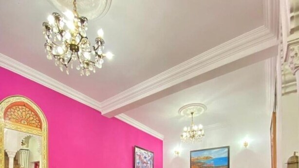 A room with a pink wall, a sofa, a small table, and a chandelier. - Riad Dar Baddi Avec 9 Suite : Marrakech (Marrakech)