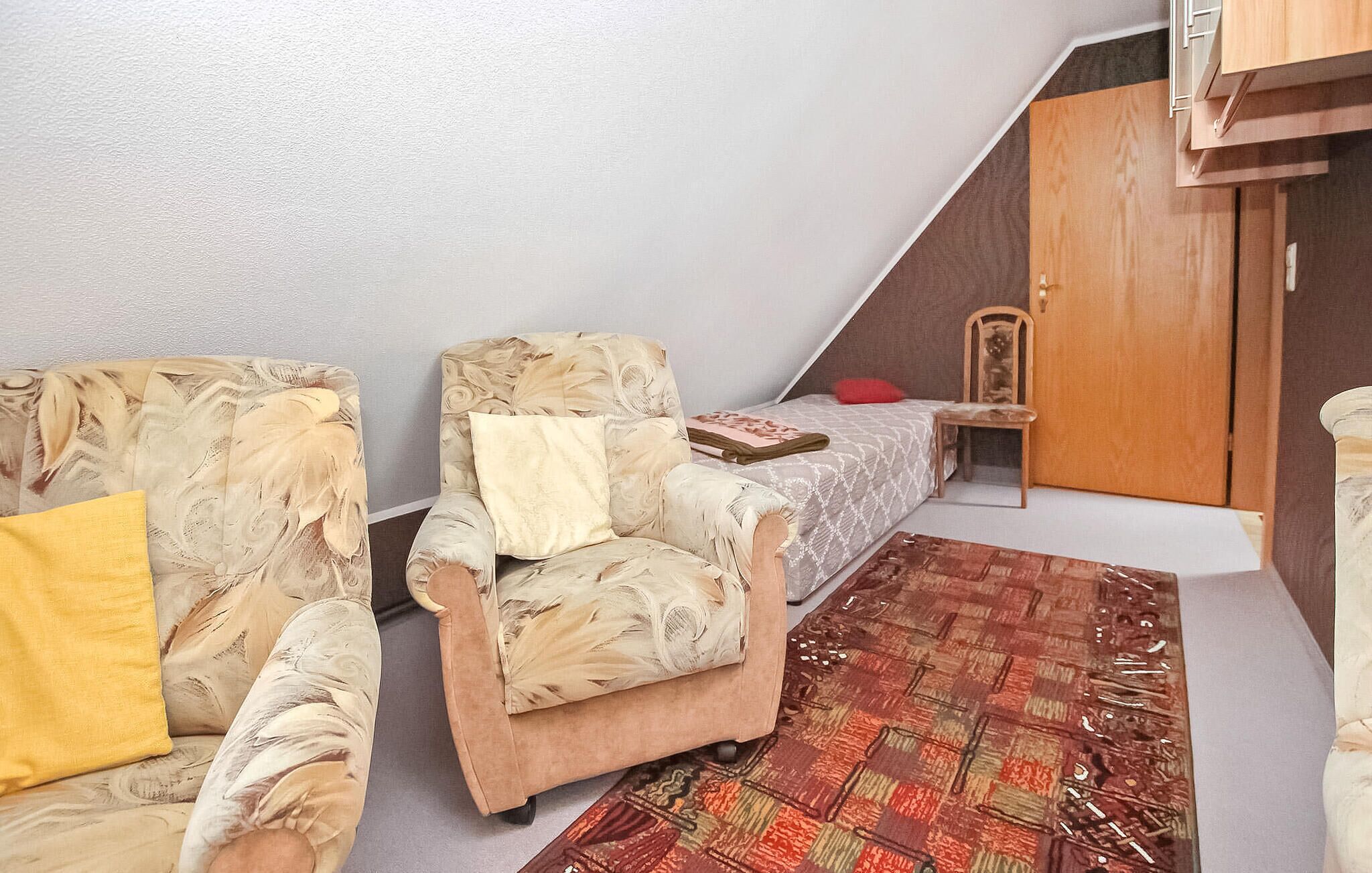 A small, cozy room with two armchairs, a small table, a patterned rug, and a wooden door.