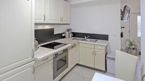 A compact kitchen with white cabinets, a stove, oven, sink, and a small refrigerator. - Ferienwohnung Hohen Sprenz (Hohen Sprenz)
