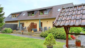 A two-story house with a sloped roof, a covered patio with outdoor furniture, and a well-maintained garden. - Stunning apartment in Stolpe/Usedom (Stolpe/Usedom)
