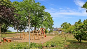A playground with wooden structures and a slide, surrounded by trees and a grassy area.