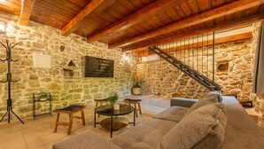 Uma sala de estar acolhedora com parede de pedra, vigas de madeira, escada e sofá.