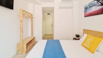 Habitació d'hotel amb un llit, una panxa de fusta, un televisor, un aparell d'aire condicionat i un quadre a la paret.