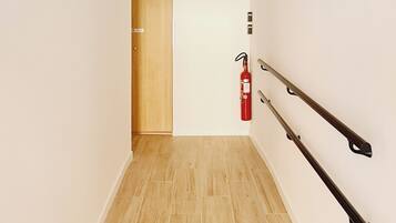 A hallway with a wooden door at the end, a fire extinguisher mounted on the wall, and a ceiling with exposed wiring.