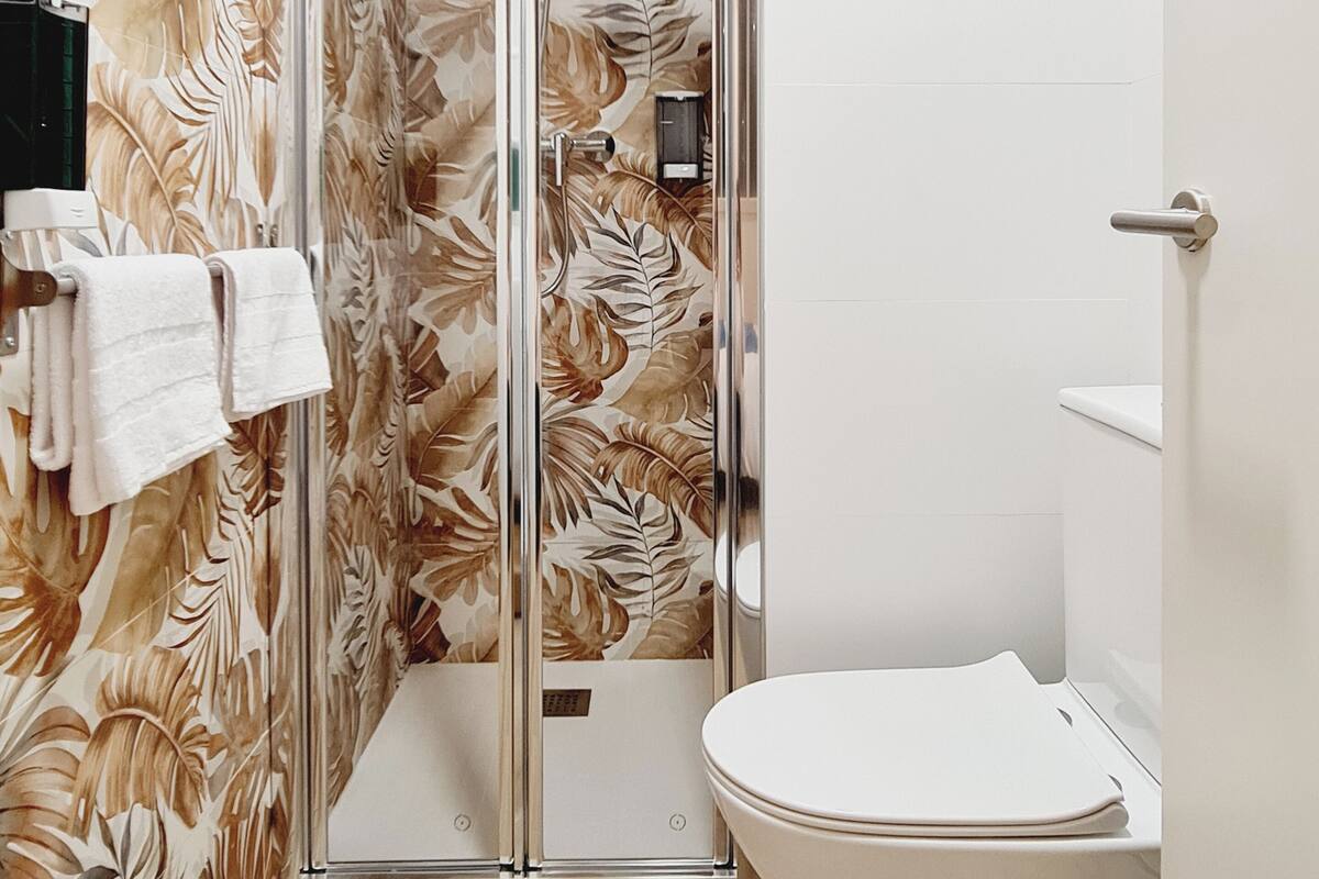 A bathroom with a shower enclosure, a toilet, and a towel rack with towels.