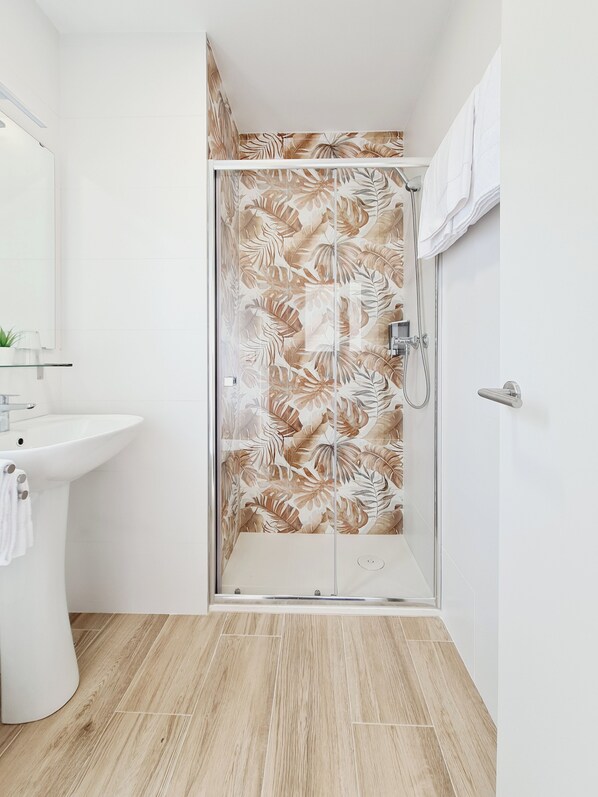 Un baño con ducha, lavamanos y espejo.