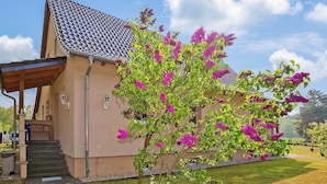 Een gebouw met een schuin dak, een overdekte veranda en een tuin met bloeiende planten.