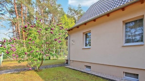 Een huis met een pannendak, een kleine tuin met een bloeiende boom, en een heldere lucht.