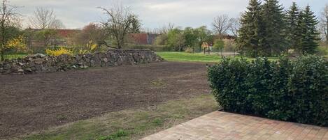 Un jardin aménagé avec un mur en pierre, une zone pavée et une haie.