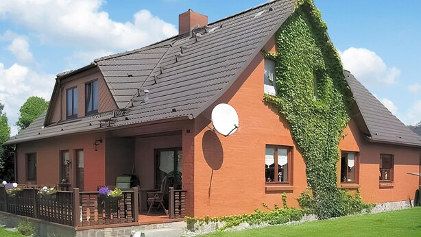 A house with a sloped roof, a covered porch, and a satellite dish. - Ferienwohnung Altenkirchen (Altenkirchen auf Rügen)