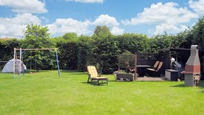 A backyard with a swing set, a lawn chair, a barbecue grill, and a tent. - Ferienwohnung Altenkirchen (Altenkirchen auf Rügen)