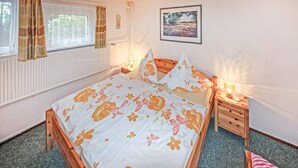 Ein Schlafzimmer mit Bett, Nachttischen, einem Fenster mit Vorhängen, einer Heizung und einem gerahmten Bild an der Wand.