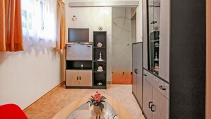 Ein kleiner Wohnbereich mit Fernseher, einer Schranke mit Regalen und einem Tisch mit einer Vase.