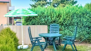 Eine Außenpatio mit einem grünen Tisch und Stühlen, einem gestreiften Sonnenschirm und einer Hecke im Hintergrund.